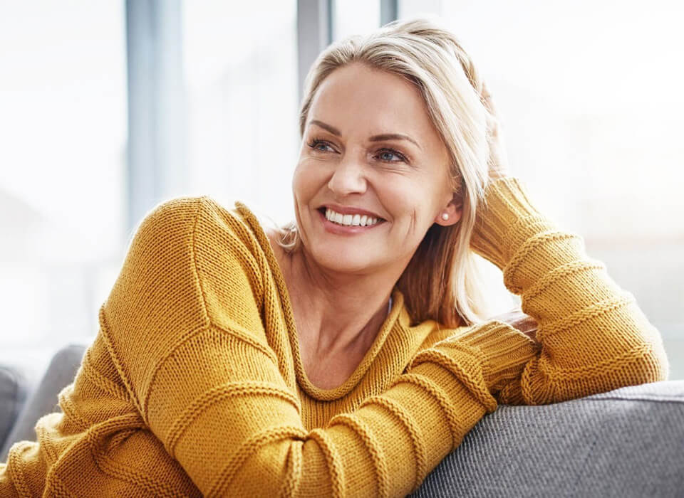 A middle aged smiling woman with grey hair wearing an yellow sweat shirt