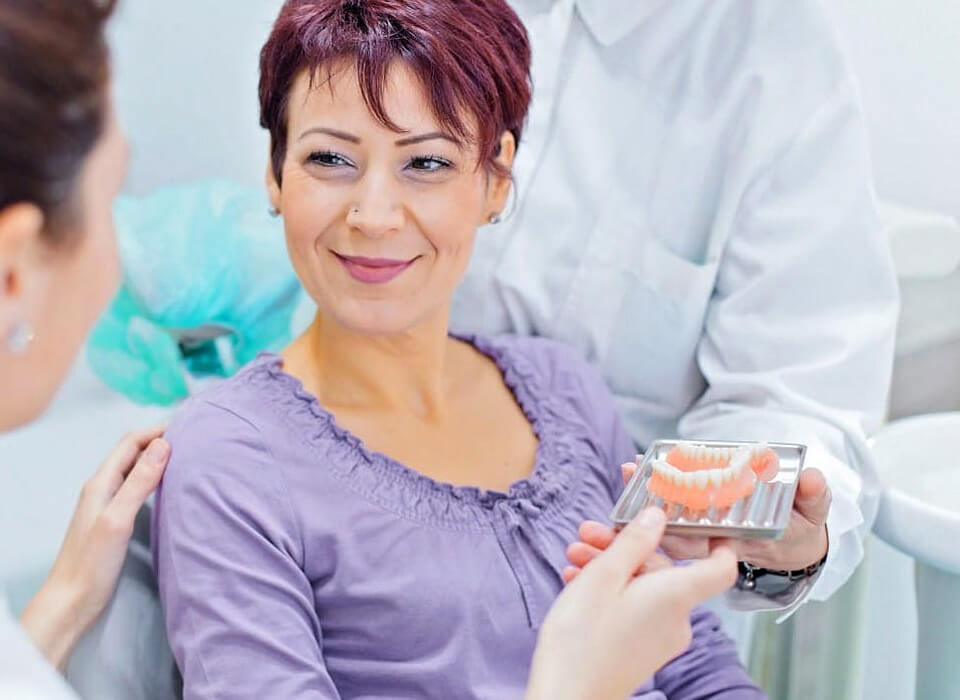A smiling woman patient with a set of dentures in front of her , which is also holding by doctor and assistant