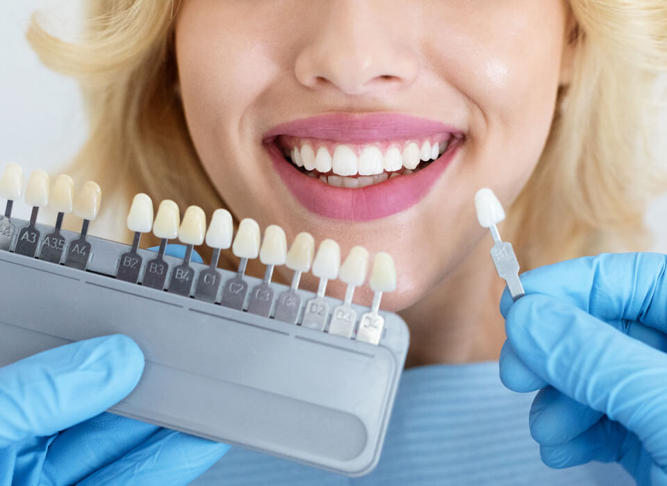 Image showing a smiling girl with open teeth and hands of doctor checking her teeth with relevant colored porcelain crown